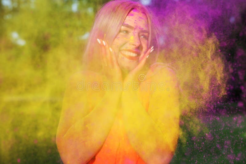 Closeup portrait of nice blonde woman having fun in a cloud of yellow and purple dry Holi paint. Closeup portrait of nice blonde model having fun in a cloud of stock images